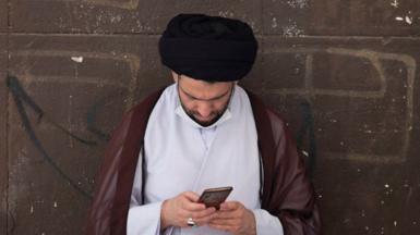 An Iranian cleric uses his smartphone