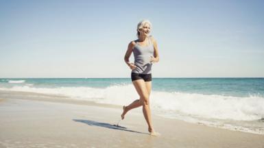 Woman with grey hair running on the beach