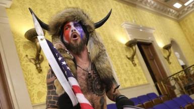 A man in horns and a fur hat, alleged to be Jake Angeli, pictured inside the Senate chamber