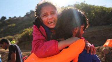 A young girl is helped moments after she arrived with other Syrian and Iraqi migrants on the island of Lesbos in 2015