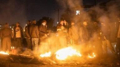 Armed community members gather around a fire to keep warm at a road block set up in Phoenix Township, North Durban, on July 15, 2021 to prevent looters from reaching the community.