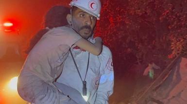 Paramedic Mohamed Mekkawy carries a girl through the street with an ambulance in the background