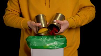 A person emptying tins into a bin
