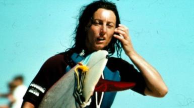 Linda Sharp holding a surfboard after competing in the French World championship in 1980