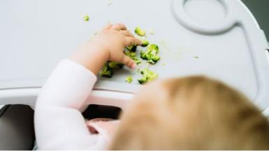 A baby with broccoli pieces in front of them