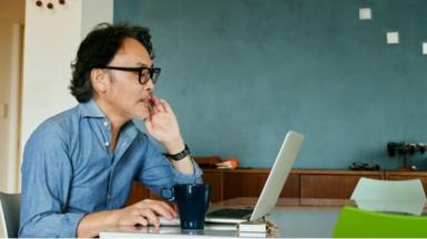 Man wearing glasses sits at desk working on laptop