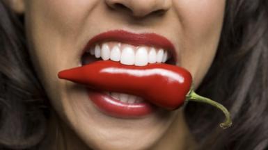 Close up of female mouth biting red chilli
