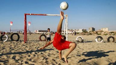 A boy kicks a ball while shooting at a football net along a beach in Libya's eastern coastal city of Benghazi on August 22, 2020.