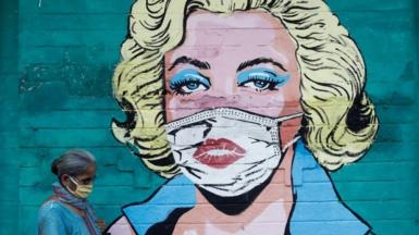 A woman wearing a protective mask walks past a graffiti depicting former American actress Marilyn Monroe wearing a mask, amidst the spread of the coronavirus disease (COVID-19), on a street in Mumbai, India, March 30, 2021.