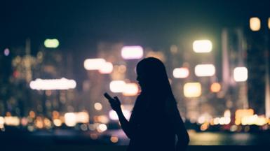 Woman holding a phone against background of bright streetlights