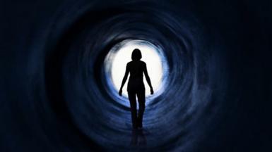 Silhouette of woman walking towards a bright light