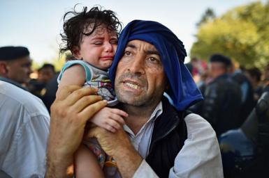 A man holds his crying child close to him as migrants force their way through police lines at Tovarnik station for a train to take them to Zagreb on September 17, 2015 in Tovarnik, Croatia.