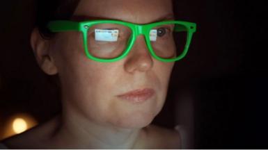 Woman in green classes stares at screen