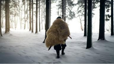 Man wearing animal skin coat walking in forest