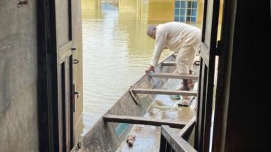 Mohammed Sani Gambo stands in a canoe. Its front is moored inside the doorway of his flooded house.