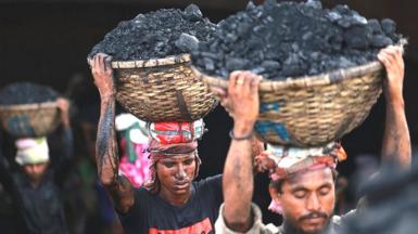 Men carrying baskets of coal on their heads in a line in Dhaka, Bangladesh