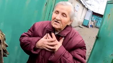 Ukrainian elderly woman with hands on chest, being persuaded to leave home on front-line