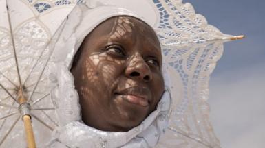 A woman dressed in white carries a matching white, lace parasol.