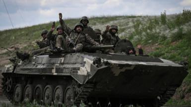 Ukrainian servicemen wave as they move towards a checkpoint near the city of Lysychansk in the eastern region of Donbas on 23 May