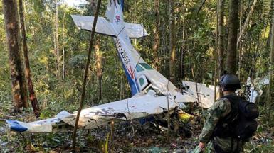 A soldier stands next to the wreckage of a plane