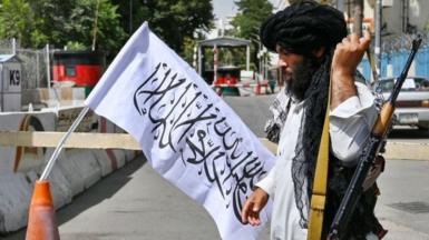 An armed Taliban fighter stands guard in Kabul next to a Taliban flag