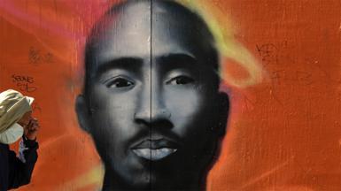 Tupac mural on a wall with orange background.