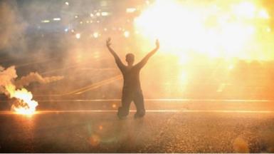 Man kneeling amidst fires in protest
