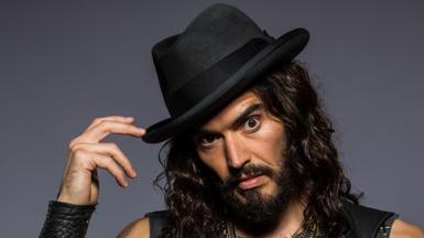 Russell Brand poses in a hat with long hair