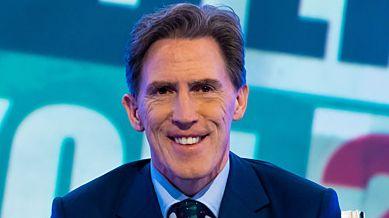 Rob Brydon wearing a suit, smiling at the screen hosting TV show Would I Lie To You