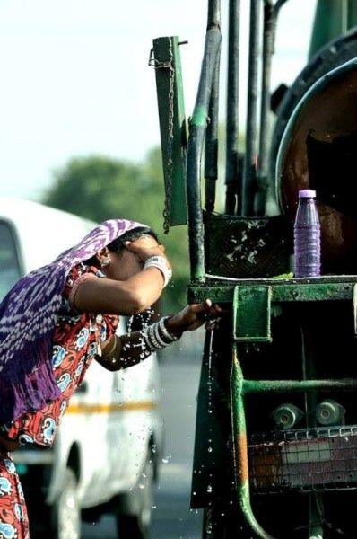 A woman cools herself from a roadside water tap