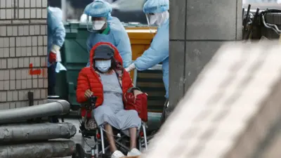 Medical workers wearing personal protective equipment suits (PPE) transferring a patient in a wheelchair at Taoyuan General Hospital,