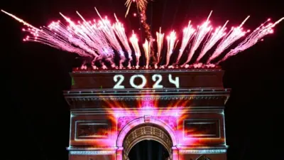 Fuegos artificiales junto al Arco de Triunfo con la palabra "2024" proyectada, en la Avenida de los Campos Elíseos, París