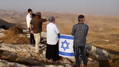 مستوطنون يحملون العلم الإسرائيلي خلال مهمة استكشافية للعثور على أراض جديدة بالقرب من مستوطنة كوخاف هاشاهار الإسرائيلية في الضفة الغربية التي تحتلها إسرائيل، 6 نوفمبر/تشرين الثاني 2022.