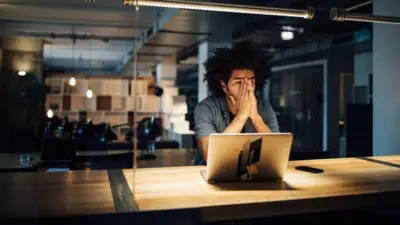 Homem no escritório diante de computador na mesa, com mãos no rosto e olhar preocupado