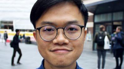 Headshot of Dr Kiwi Tang standing in a street. He is wearing round glasses and has short black hair.
