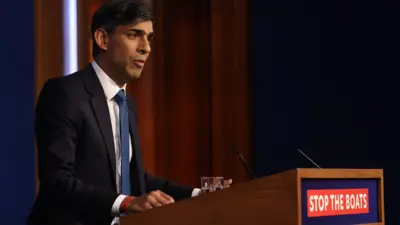 Rishi Sunak at a lectern with the slogan Stop the Boats