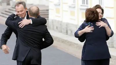 بلير وبوتين وزوجاهما يتعانقون خلال زيارة لرئيس الوزراء البريطاني وزوجته إلى مدينة سانت بطرسبيرغ الروسية في منتصف شهر يوليو/تموز عام 2006.