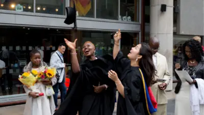 Pikin wey dey hold flowers while graduates celebrate
