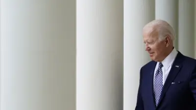 Biden caminhando na Casa Branca, sorrindo timidamente