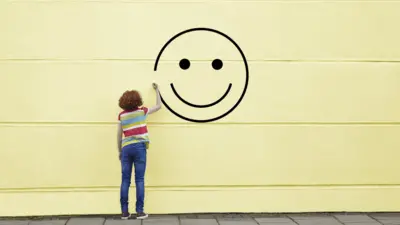 Menina de costas desenha rosto feliz na parede