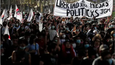 Pessoas carregam faixa em manifestação com o texto "Libertad a lxs presxs políticxs"