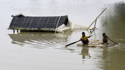 روستاییان هندی با کمک یک قایق در منطقه سیل‌زده آسام به مکان امنی منتقل می‌شوند