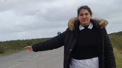La maestra María Domínguez al borde de la carretera extiende su brazo en señal de que pide un aventón.