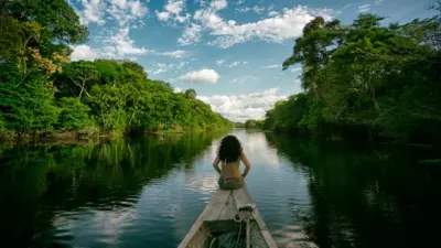 Una indígena sentada sobre una canoa en un río amazónico.