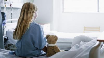 Young girl sitting on a hospital bed with a teddy bear next to her