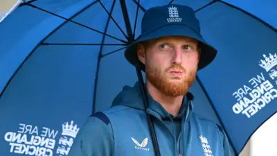 England captain Ben Stokes looks on from under an umbrella as rain falls at Old Trafford
