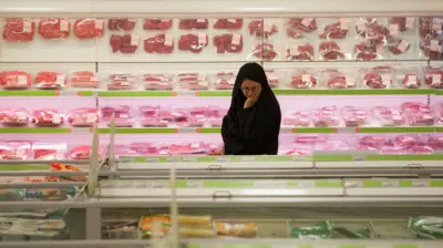 یک زن ایرانی در بخش گوشت یک سوپرمارکت در تهران به محصولات نگاه می‌کند