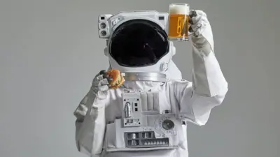 فضانوردی یک آب جو و همبرگر در دست دارد