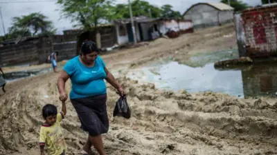 Uma mulher caminha com o filho em Piura, após as enchentes de 2017