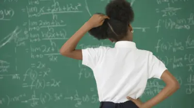 ሰሌዳው ላይ የተጻፈውን የሂሳብ ስሌት የምትመለከት ተማሪ